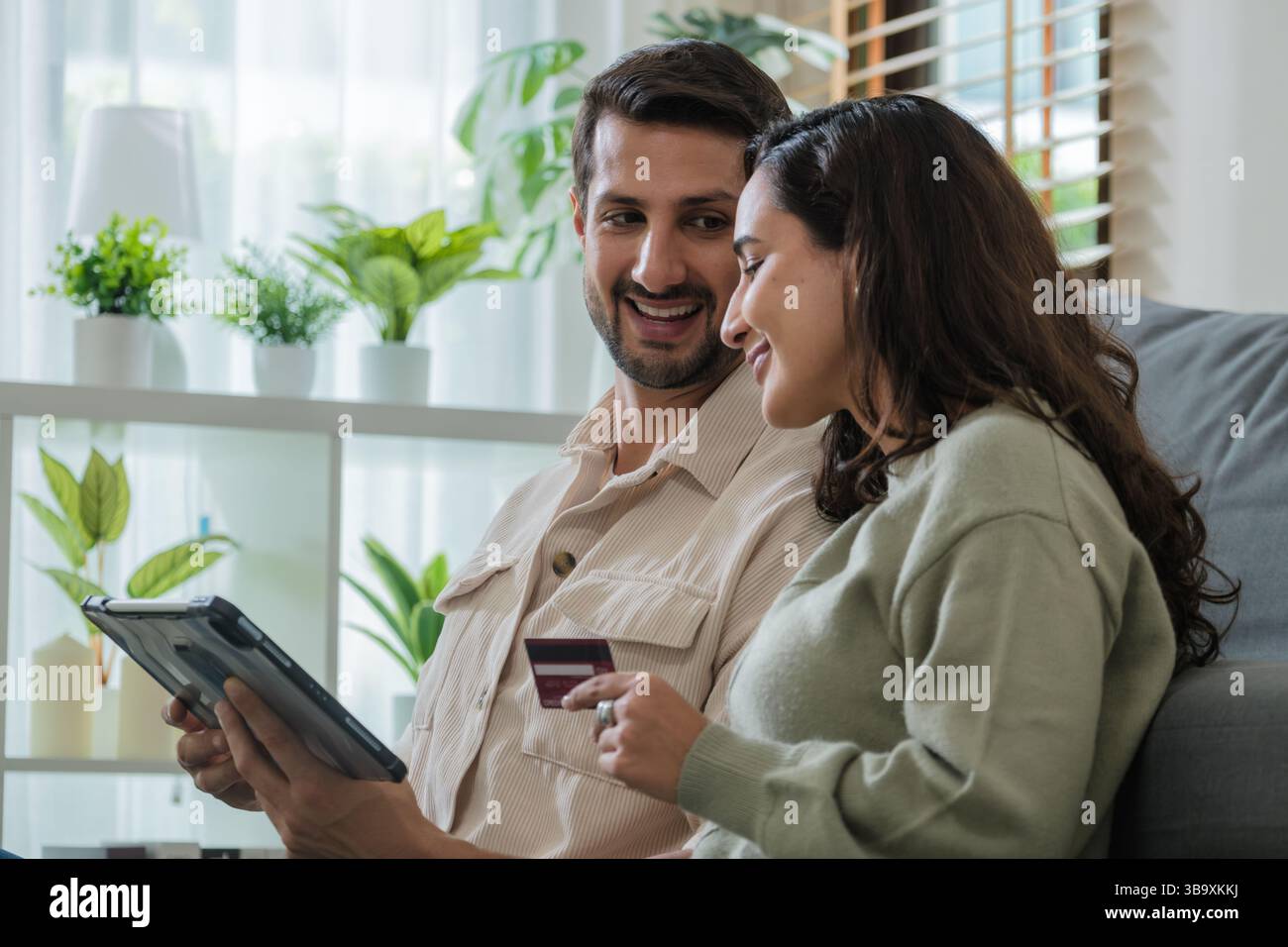 Couple hispanique utilisant la tablette et la carte de crédit pour magasiner en ligne via l'application e-commerce, faire le paiement et la navigation plate-forme moderne avec des codes promo et d Banque D'Images