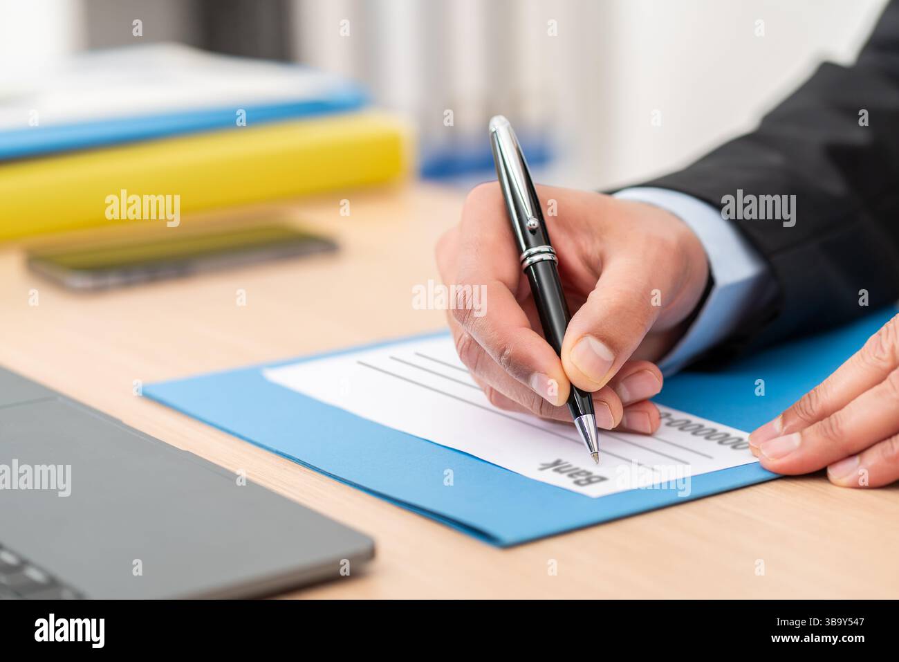 Gros plan d'un homme d'affaires remplissant un chèque bancaire assis sur un bureau au bureau Banque D'Images