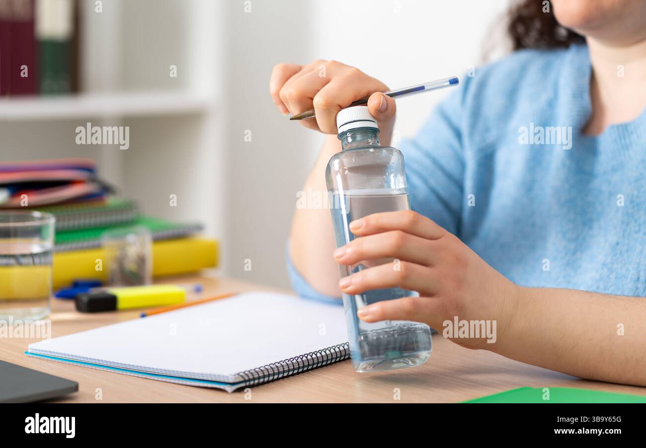 Heureuse étudiante ouvrant une bouteille d'eau assise dans le salon à la maison Banque D'Images