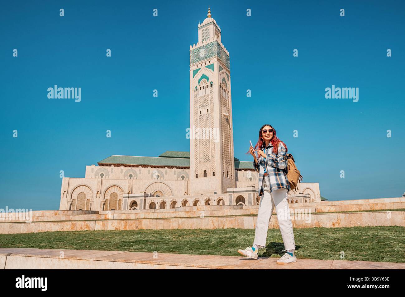 Jeune touriste marchant dans l'immense cour de la mosquée Hassan II à Casablanca, Maroc, à l'aide d'une application de carte sur smartphone Banque D'Images