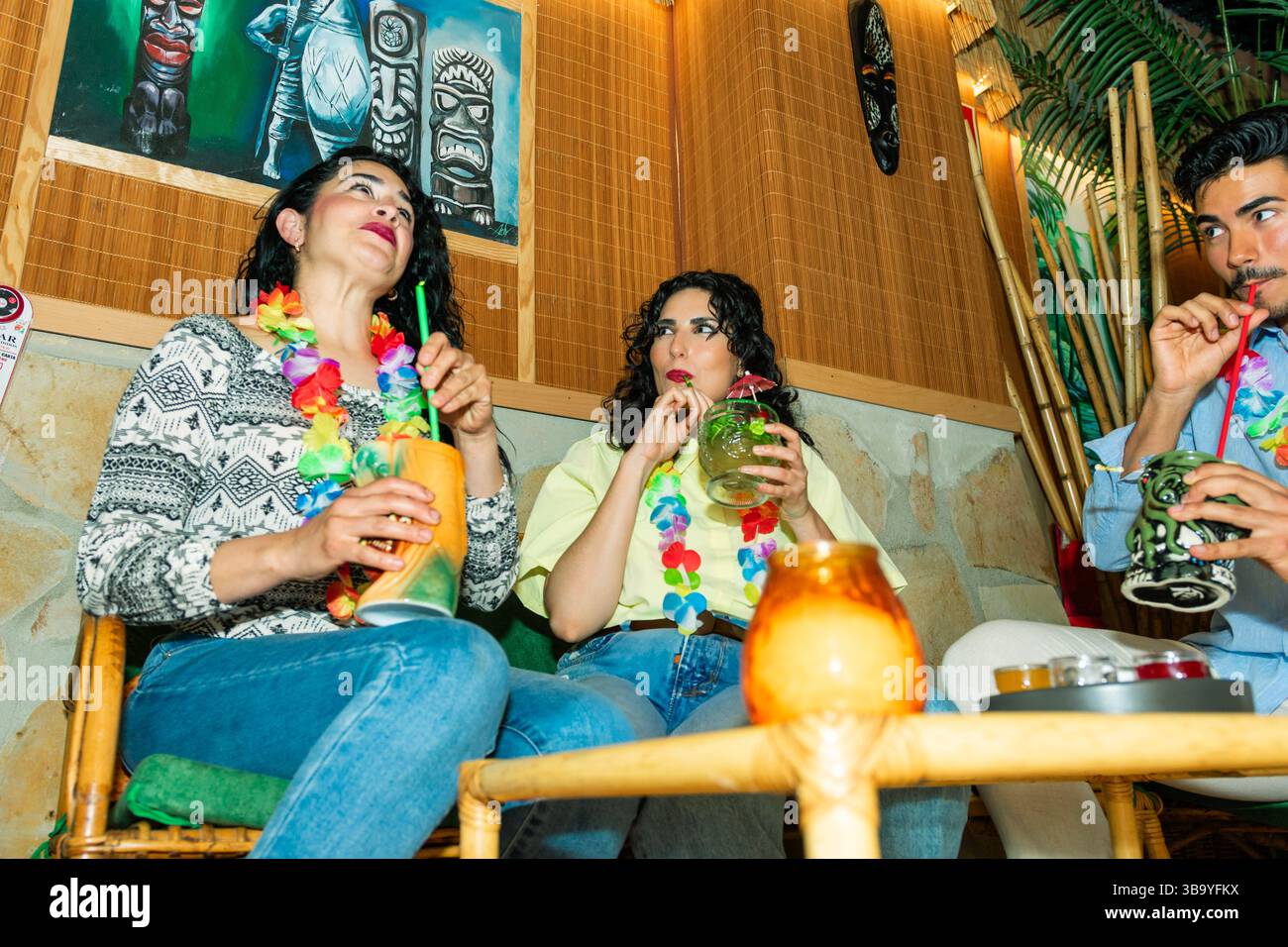 Trois amis se détendent et dégustent des cocktails tropicaux colorés dans un bar tiki Banque D'Images