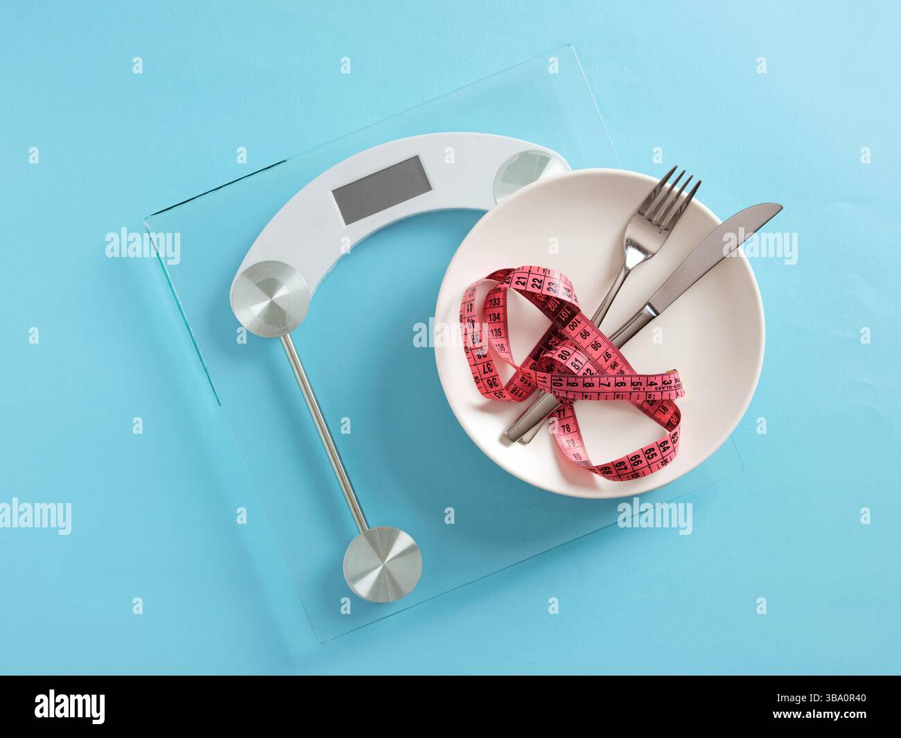 Concept de régime alimentaire. Ruban à mesurer reposant sur la plaque sur une balance numérique placée sur un fond bleu. Banque D'Images