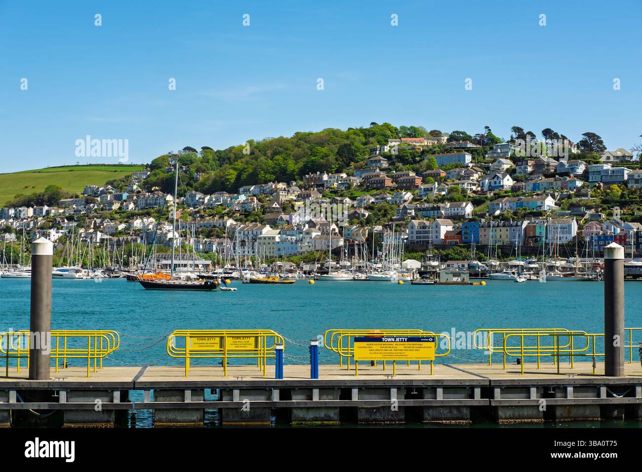 Une vue depuis la jetée de la ville, un ponton dans un port rempli de voiliers et autres navires. La jetée a des garde-corps jaune vif Banque D'Images