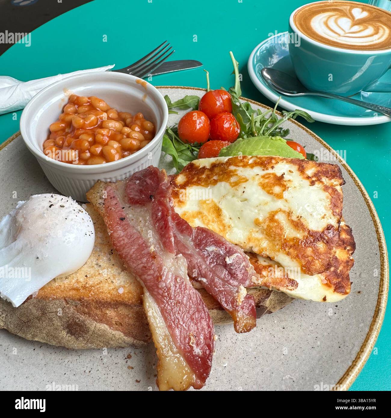 Café blanc plat avec petit déjeuner anglais complet sain sur la table turquoise. Comprend oeuf poché, bacon, pain grillé, halloumi, haricots, et des tomates. Banque D'Images
