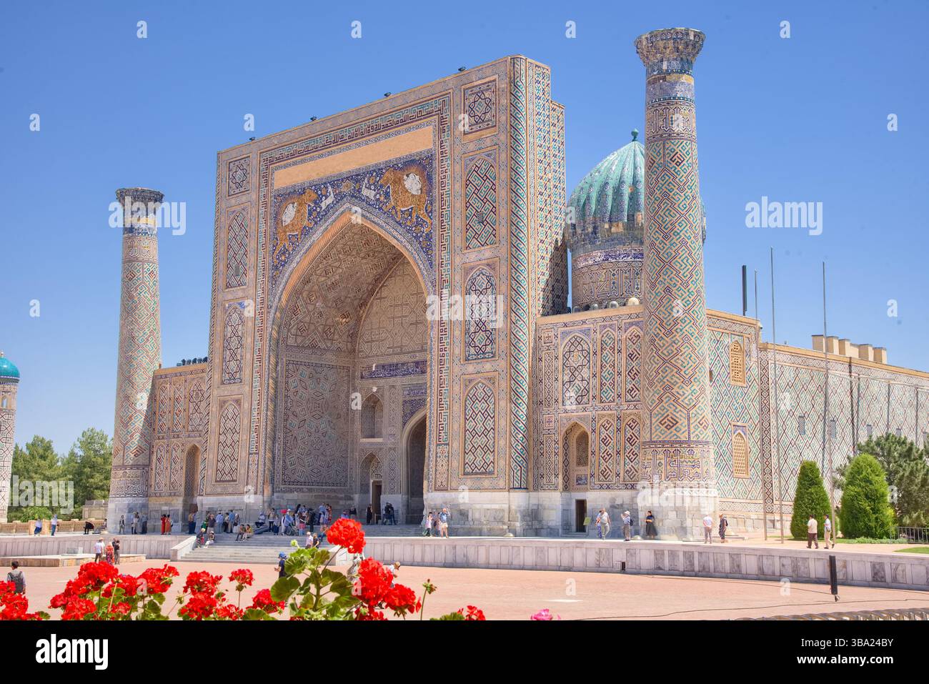 Dôme, tours de minaret et façade de la Madrasa Sher-Dor dans Registran Square Samarcande Ouzbékistan avec des fleurs rouges cadre partiel Banque D'Images