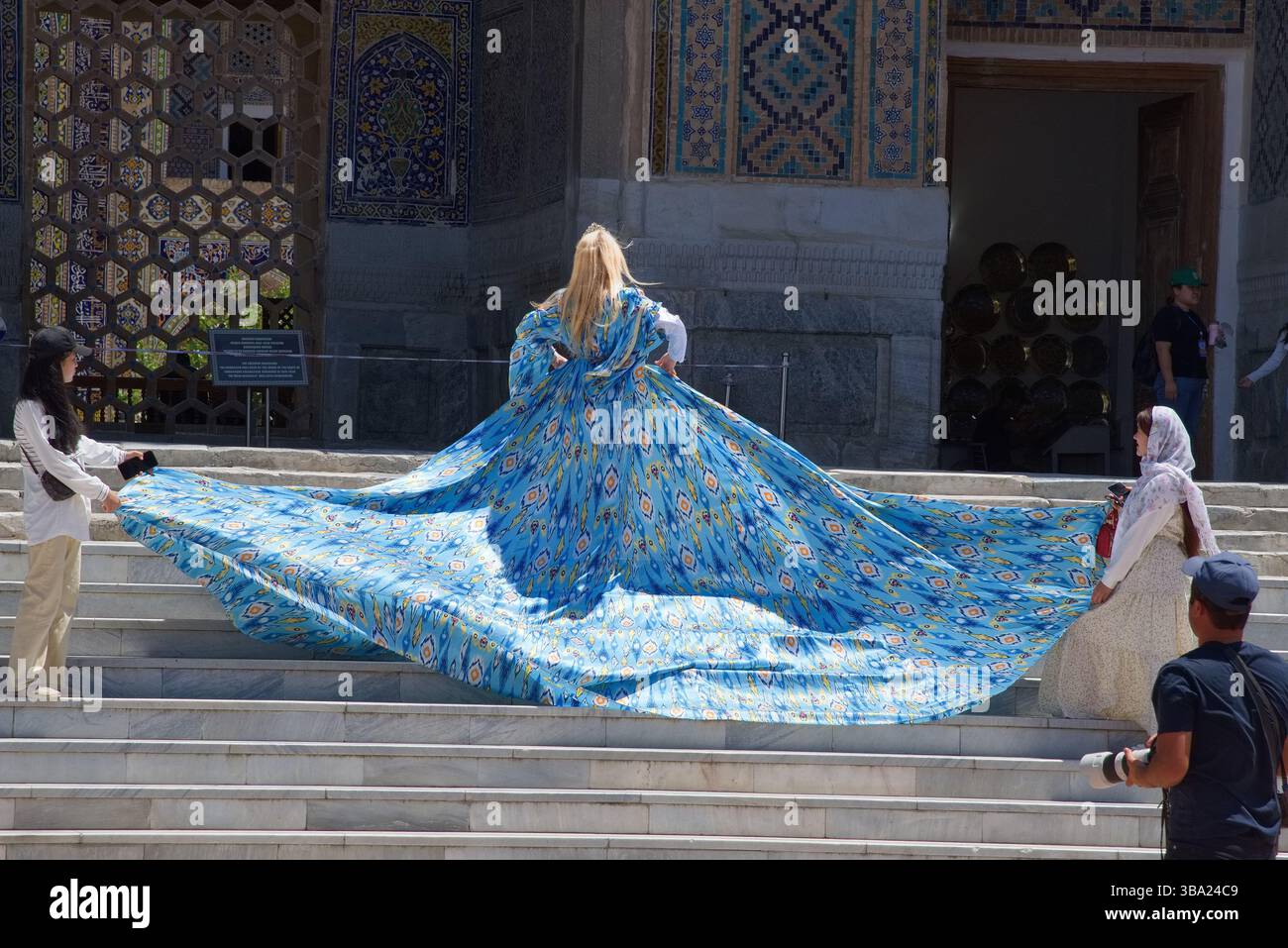 Femme blonde en robe de princesse bleue et deux femmes en foulard se préparent pour une séance photo à Registan Square, Samarcande, Ouzbékistan Banque D'Images