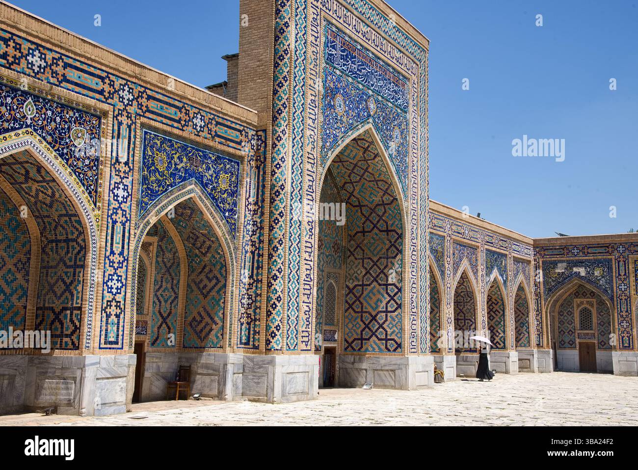 Une façade ornée de mosaïque et décorée et des arches avec femme avec un parapluie dans la madrasa Tilya-Kori sur la place Registan Samarcande en Ouzbékistan Banque D'Images