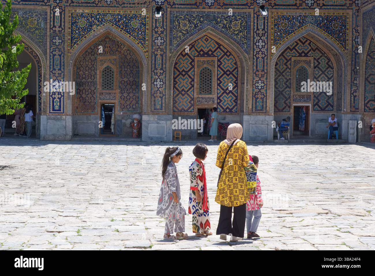 Femme en foulard avec trois enfants en tenue traditionnelle dans la Madrasa Tilya-Kori dans Registan Square Samarkand en Ouzbékistan Banque D'Images