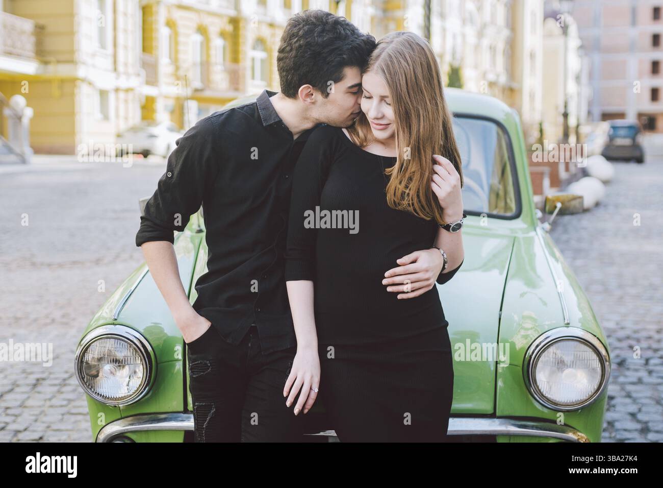 Jeune couple multiracial, hommes et femmes hétérosexuels amateurs et étudiants. Belle des modèles posant debout près d'une voiture rétro dans la ville. Habillé Banque D'Images