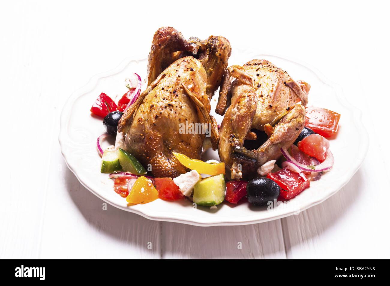 Caille entière cuite et salade de légumes frais dans une assiette blanche sur la table avec serviette verte Banque D'Images Caille entière cuite et salade de légumes frais dans une assiette blanche sur la table avec serviette verte Banque D'Images