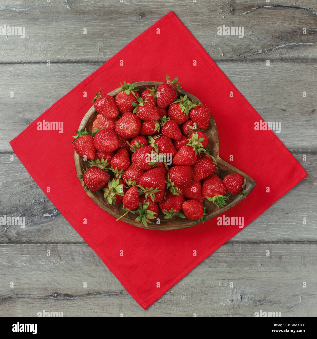 Vue de dessus, bol en bois sculpté avec des fraises sur nappe rouge et bureau en bois gris, Liptovsky Hradok, Slovaquie, Europe Banque D'Images