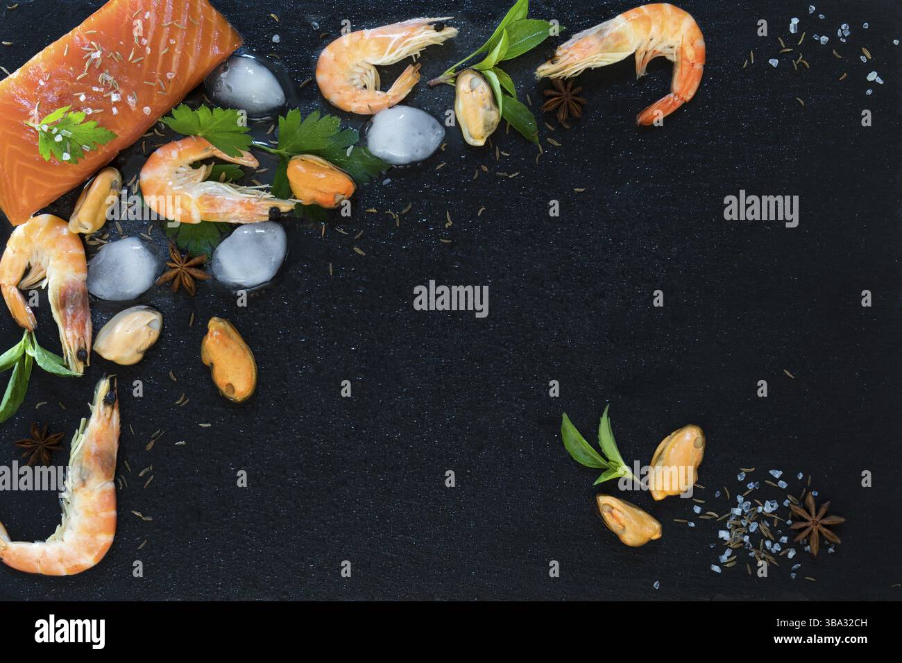 Préparation de fruits de mer frais dans la cuisine avec filet de saumon gastronomique, crevettes roses et moules entourées de glace, herbes fraîches et épices sur pierre noire BA Banque D'Images