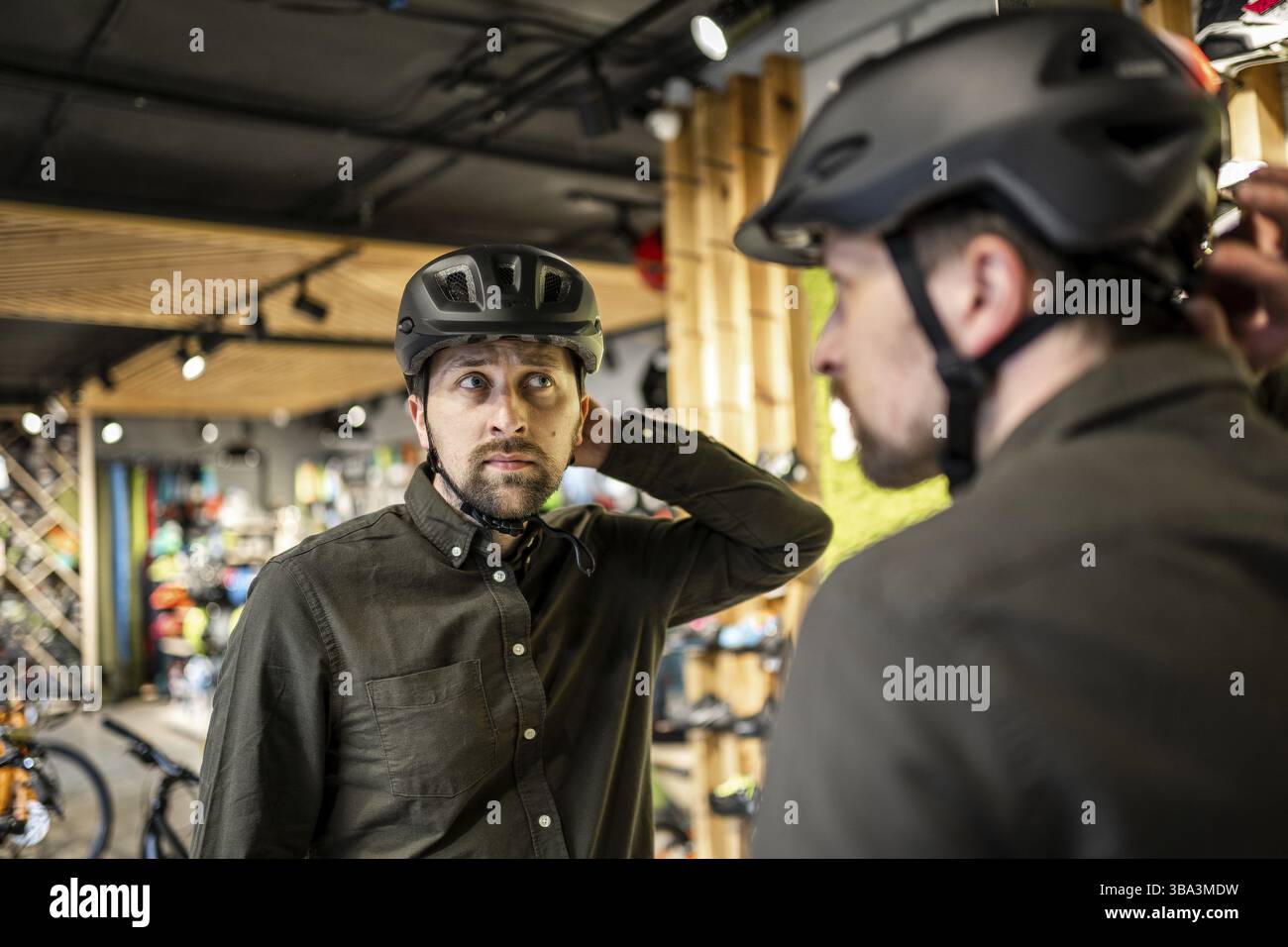 Un jeune homme est venu au magasin de vélos.Il mesure le casque.Un homme choisit un casque dans un magasin d'équipement sportif.Achat d'un nouveau casque de sport.Crème anglaise Banque D'Images