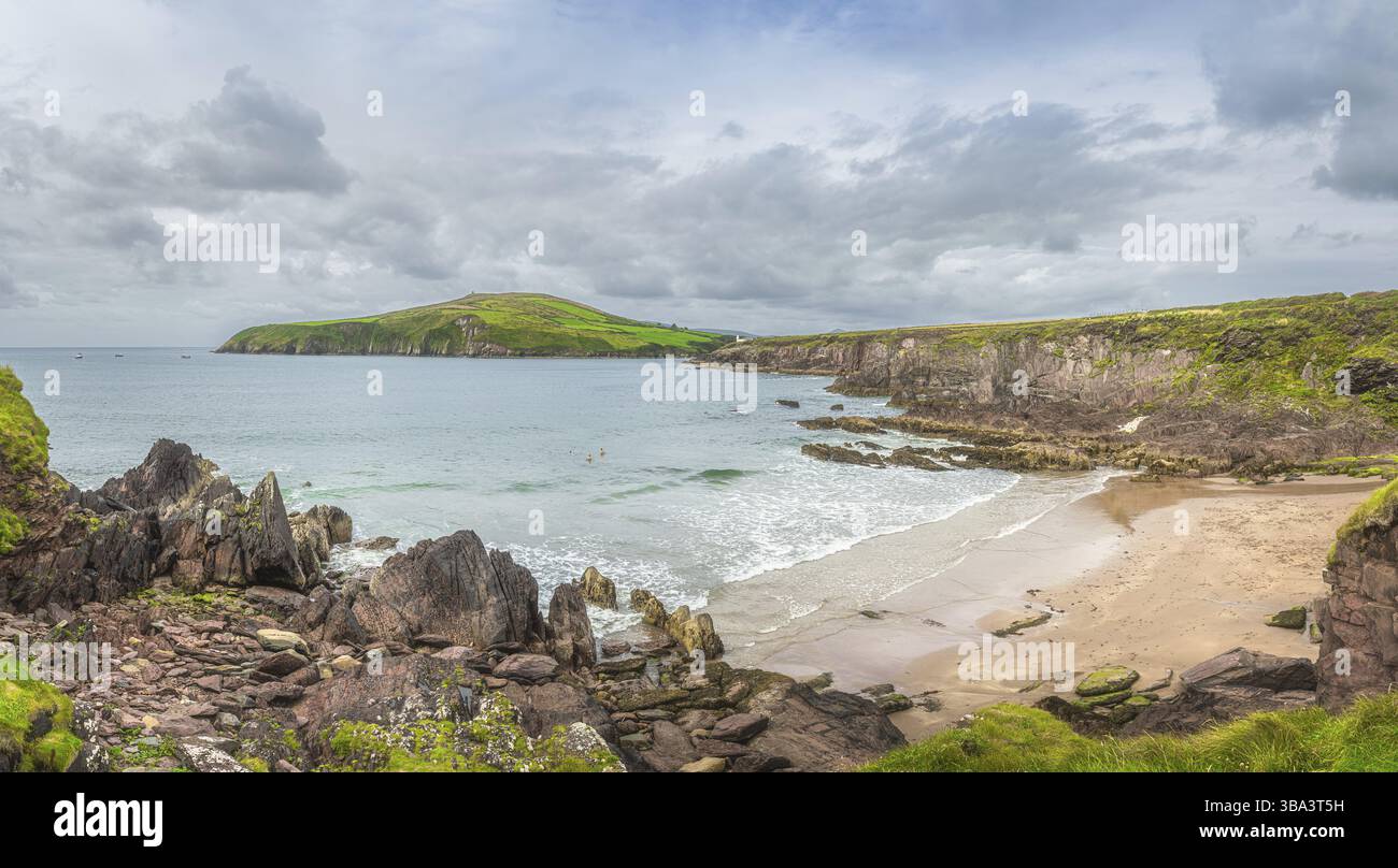 Phare de Dingle guidant les bateaux de pêche de retour. Les gens nagent dans l'eau froide de l'océan Atlantique. Plage cachée entre falaises, Kerry, Irlande, Europ Banque D'Images