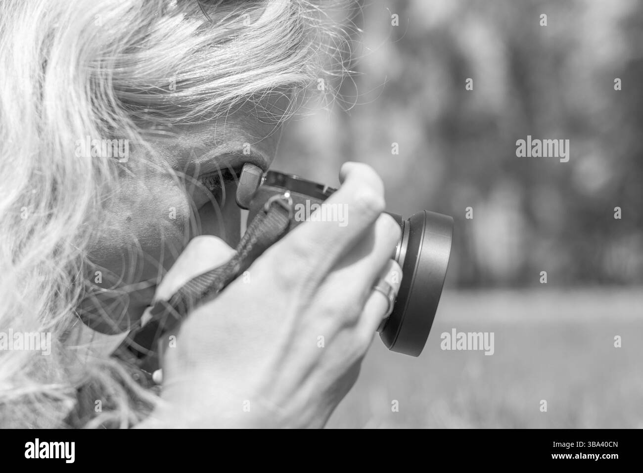 Femme photographe professionnelle prenant en plein air avec un objectif à focale fixe, lors d'une journée ensoleillée dans le parc de printemps. Noir et blanc. Faible profondeur de champ Banque D'Images