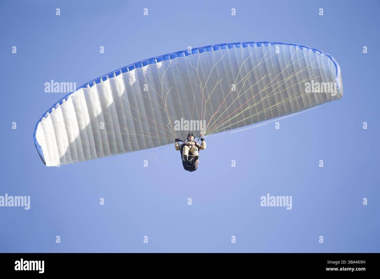 Ein Gleitschirm fliegt in den Himmel unter einem mehrfarbigen Gleitschirm. Mann unter Fallschirm Banque D'Images