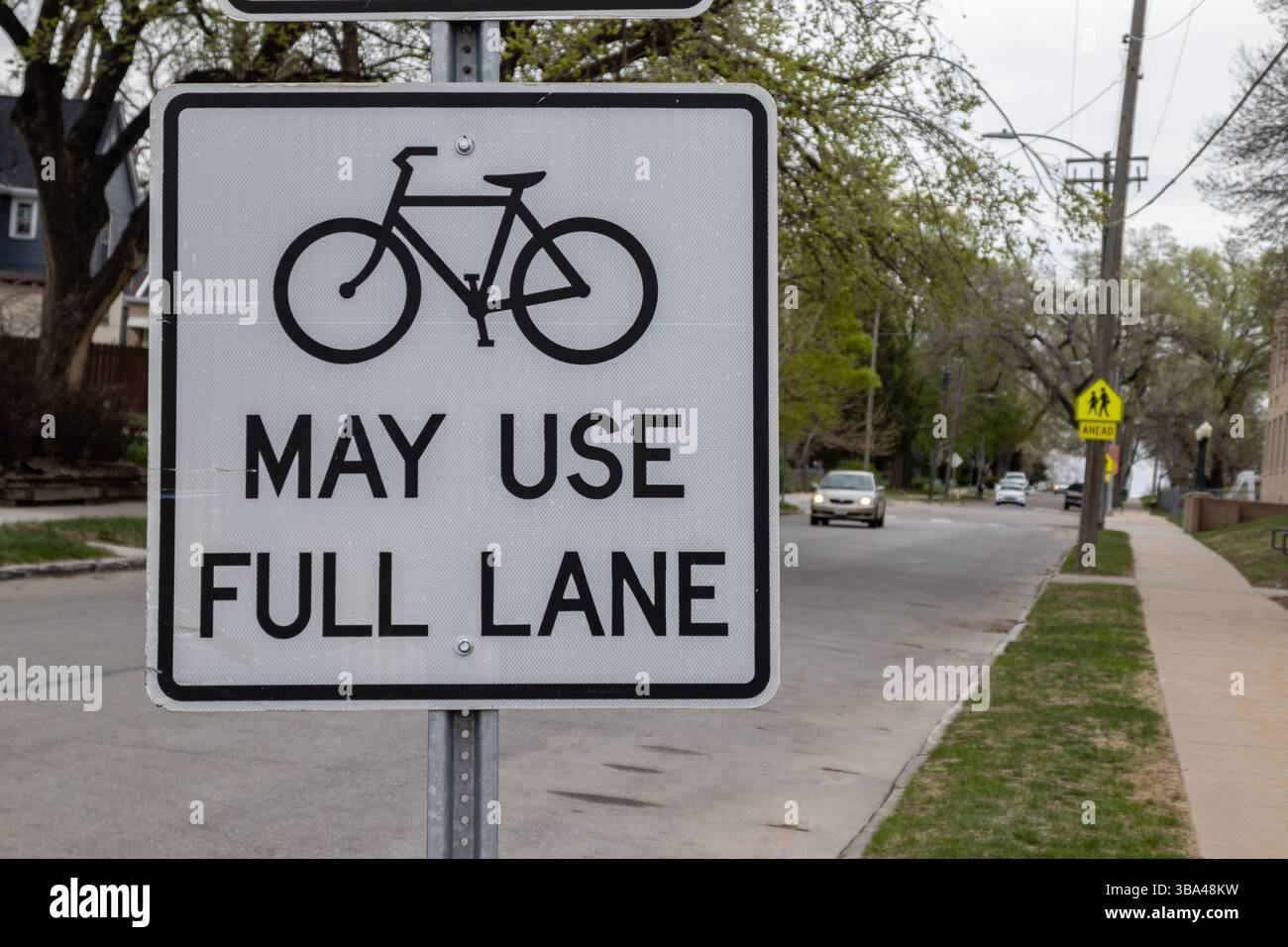 Un panneau près d'une rue résidentielle à Omaha, Nebraska, États-Unis, indique aux automobilistes que les vélos peuvent utiliser la voie pleine. Message pour la sécurité routière pour les cyclistes. Banque D'Images