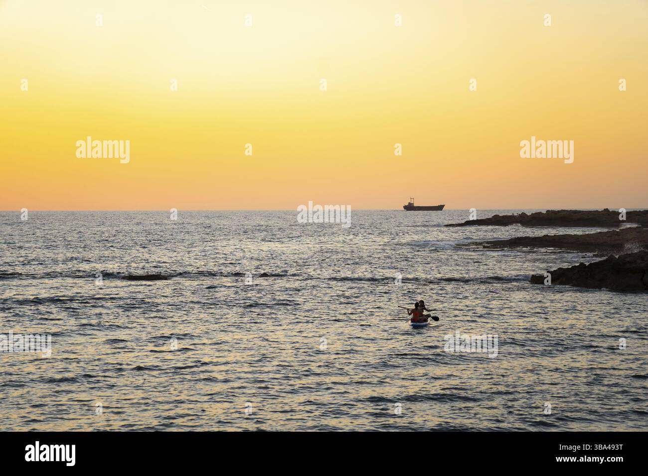 Deux filles s'assoient à bord dans la mer méditerranée tranquille au coucher du soleil dans la ville de paphos à chypre. Silhouettes de 2 filles pagayant sur paddle board à Banque D'Images