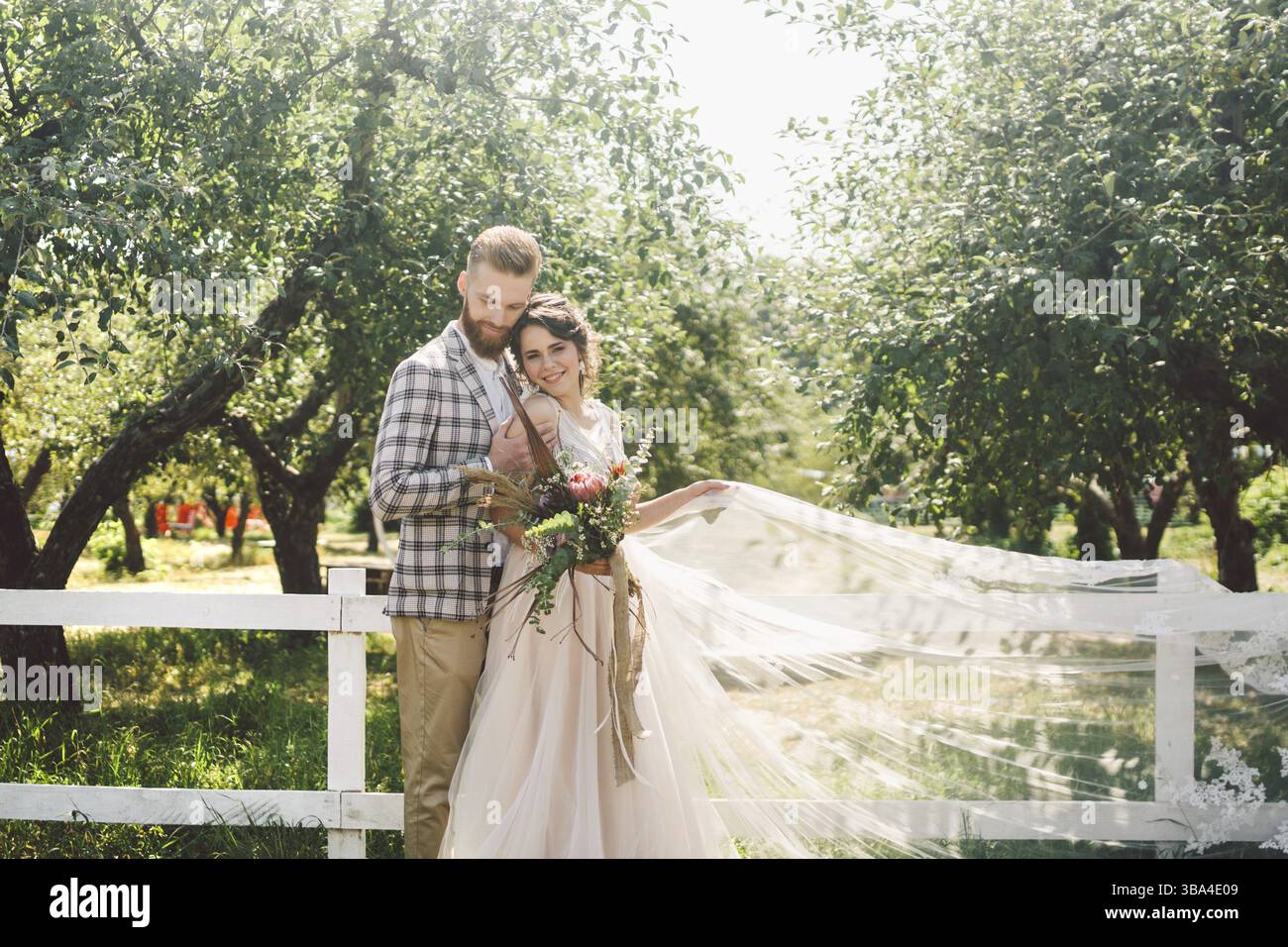 Couple caucasien dans l'amour mariée et marié debout dans étreinte près de bois blanc, clôture rurale dans le parc d'un verger de pommiers. le thème est portrait de mariage et être Banque D'Images