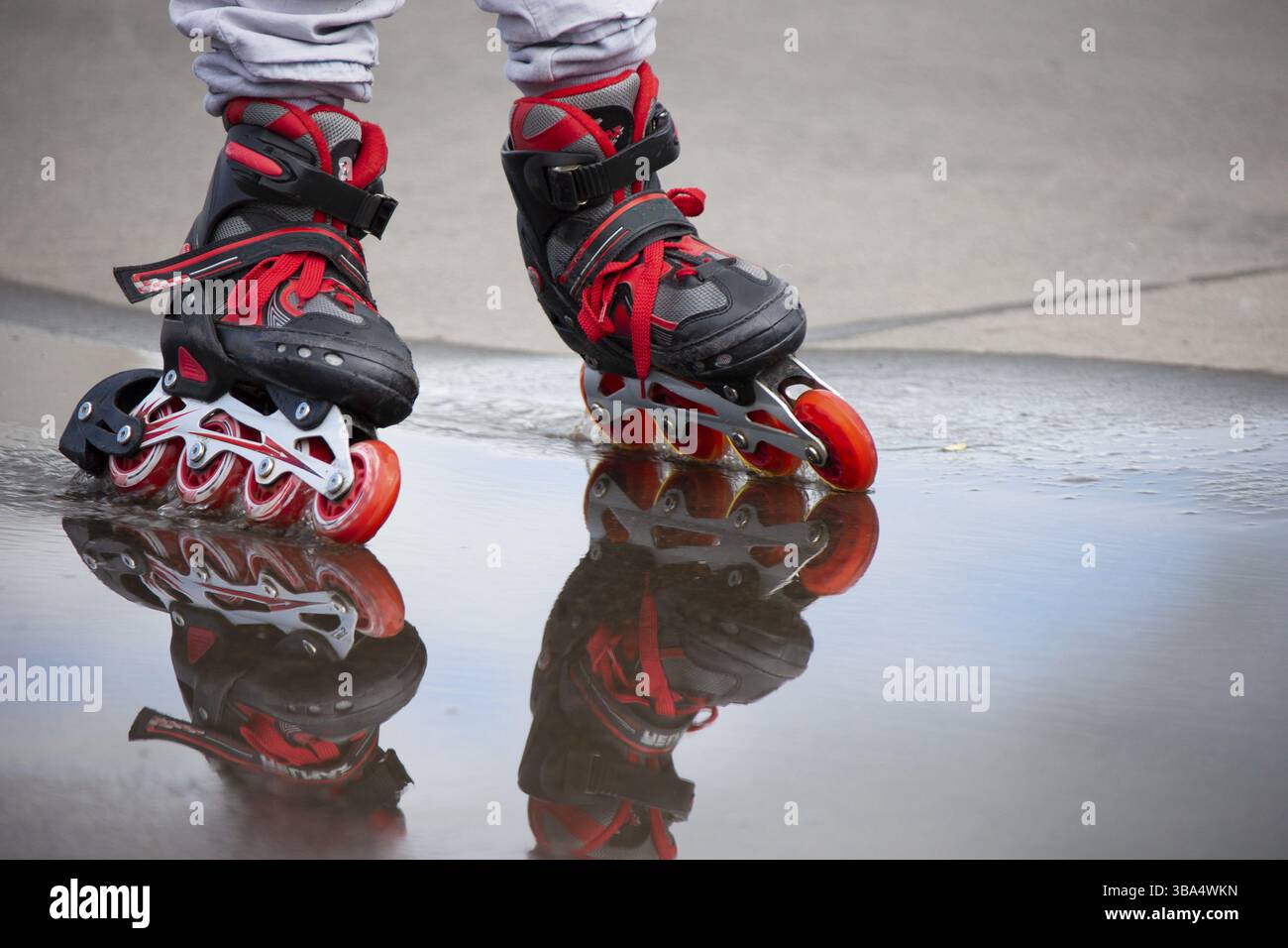 Patin à roulettes. Les jambes des patins à roulettes traversent une flaque Banque D'Images