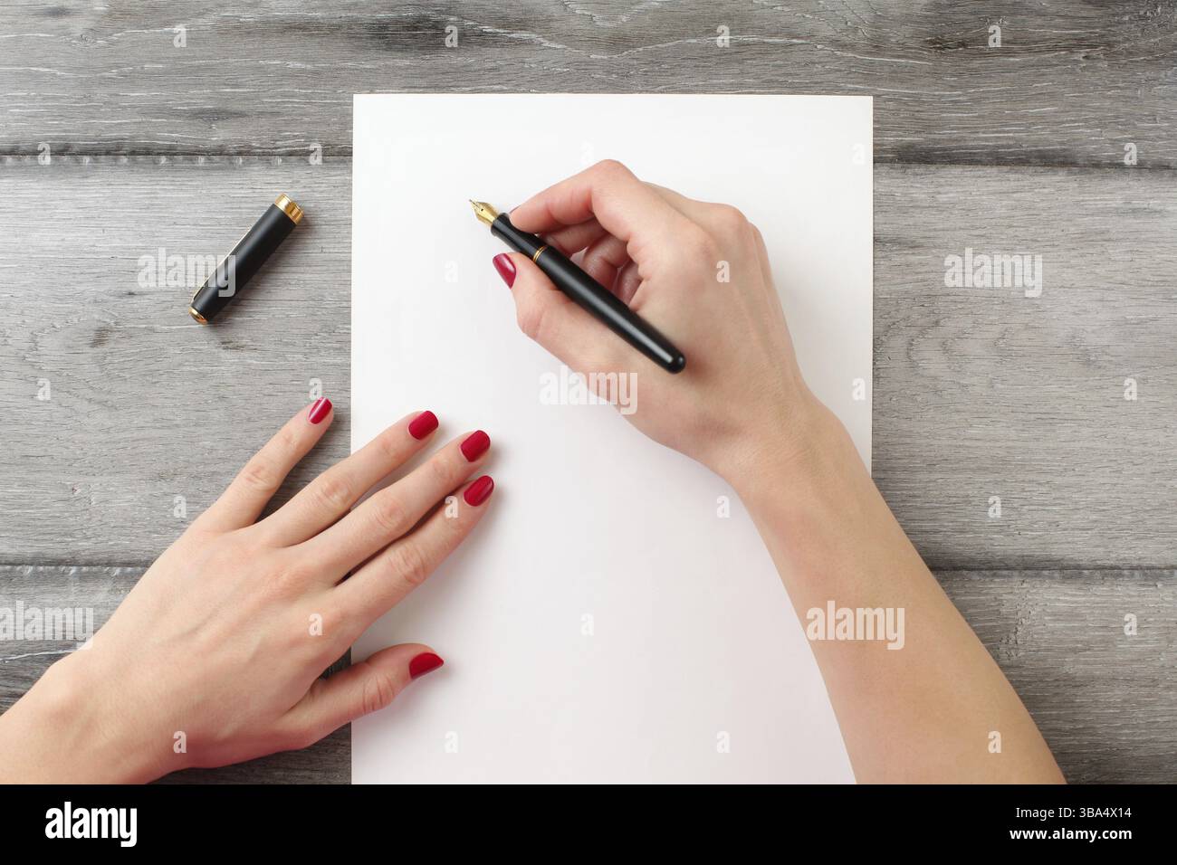Vue de dessus de woman's hands avec red nails, tenant un stylo à encre noire avec fontaine en or, prêt à écrire quelque chose sur la feuille de papier vide fixant Banque D'Images