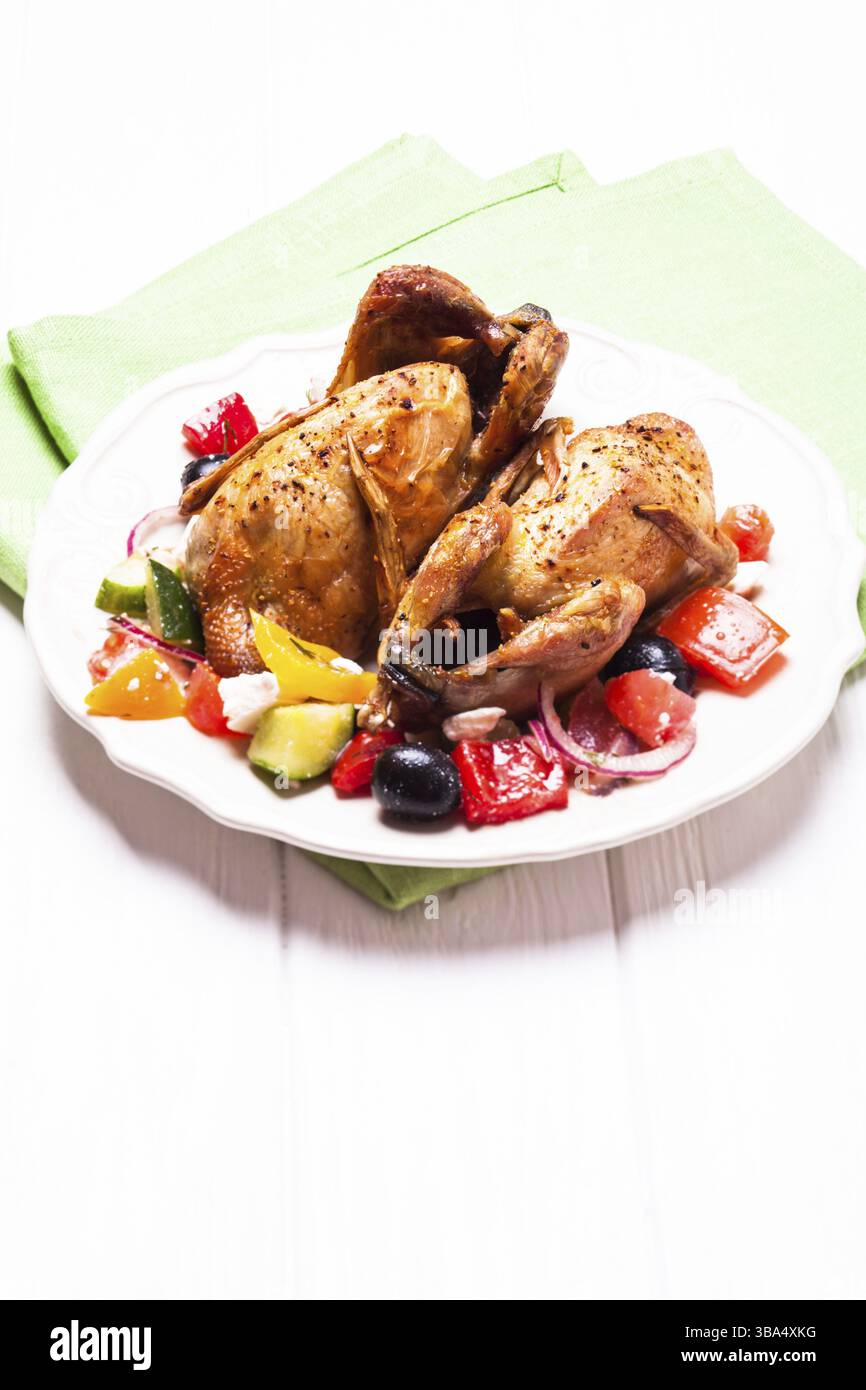 Caille entière cuite et salade de légumes frais dans une assiette blanche sur la table avec serviette verte Banque D'Images Caille entière cuite et salade de légumes frais dans une assiette blanche sur la table avec serviette verte Banque D'Images