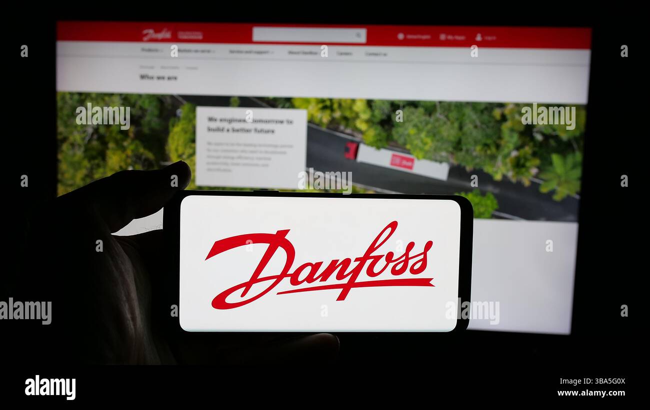 Dans cette illustration photo, une personne tient un téléphone portable avec le logo de la société danoise de chauffage-climatisation Danfoss COMME sur l'écran en face de la page Web. Banque D'Images