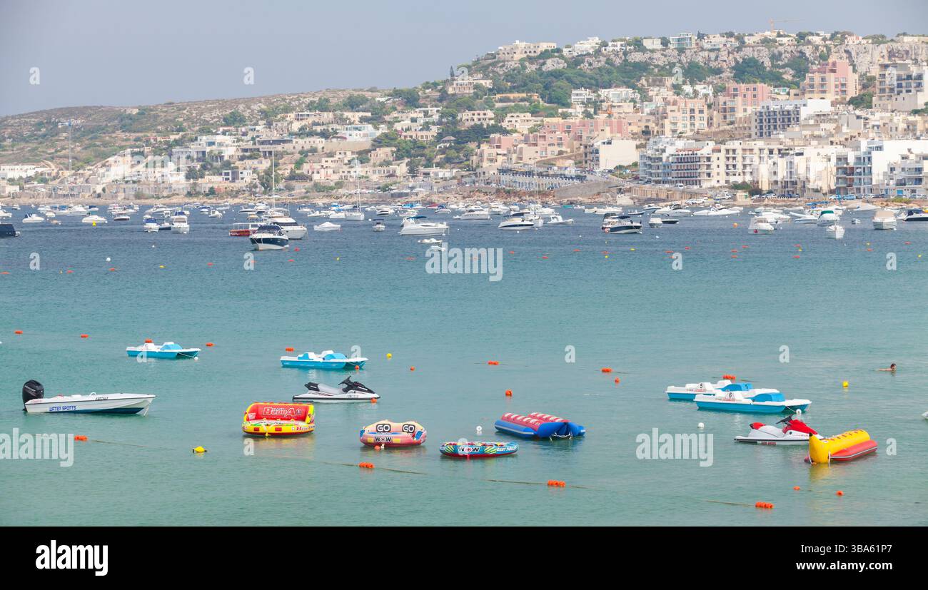 Mellieha, Malte - 29 août 2019 : une vue panoramique sur la plage avec des bateaux gonflables colorés, des eaux côtières bleues claires et une ville balnéaire animée Banque D'Images