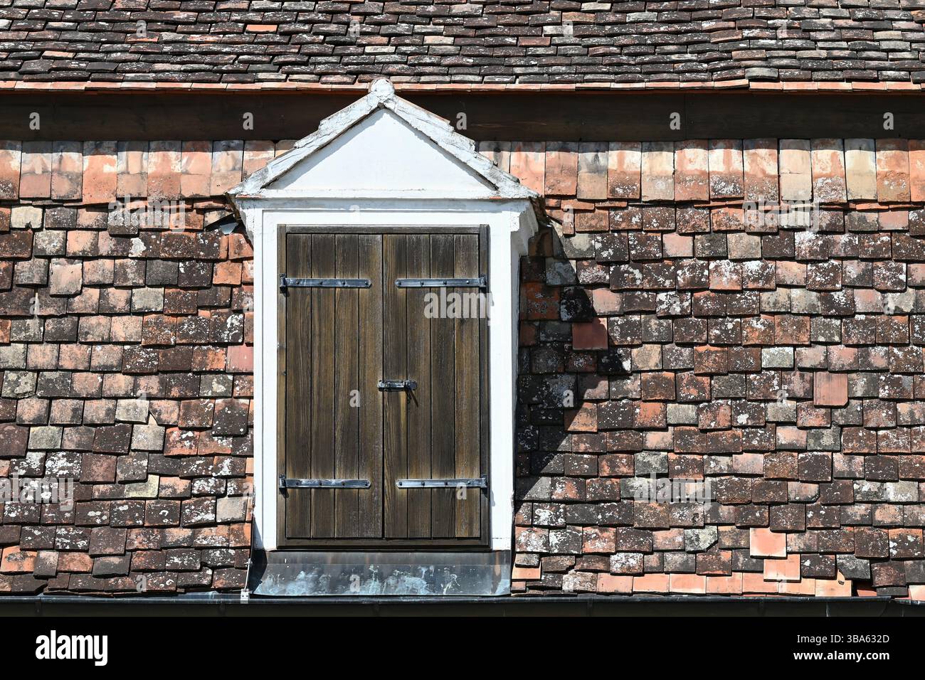 Lucarne vintage avec volets en bois fermés sur toit en tuiles rustiques en terre cuite vieillie Banque D'Images