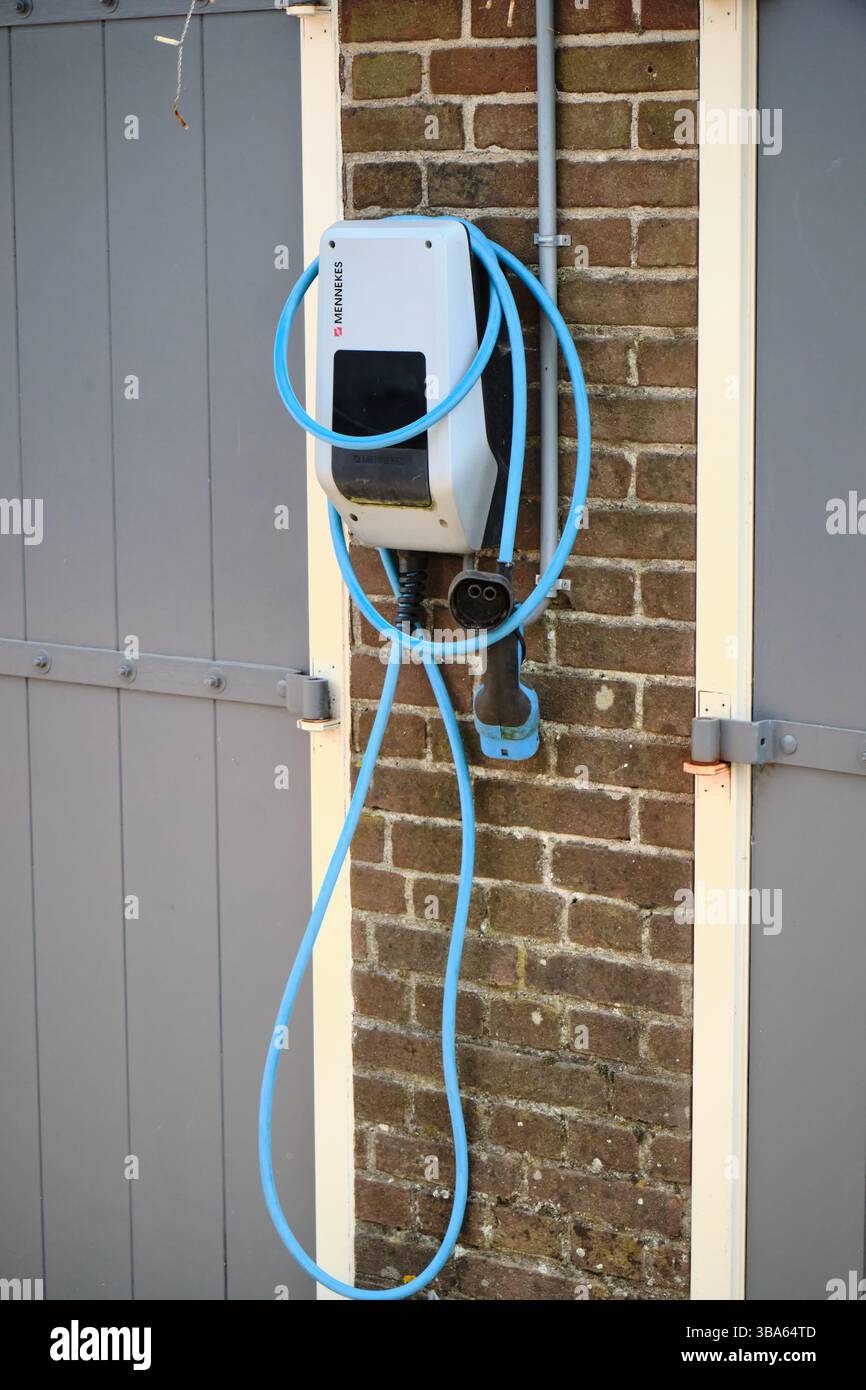 21 avril 2025 - Puttershoek-pays-Bas : borne de recharge pour véhicules électriques montée sur un mur de garage en briques, avec câble bleu, montrant local EV infras Banque D'Images