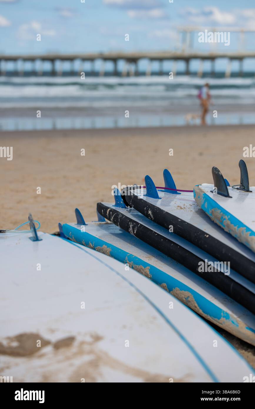 Planches de surf empilées sur la plage avec océan et jetée en arrière-plan Banque D'Images