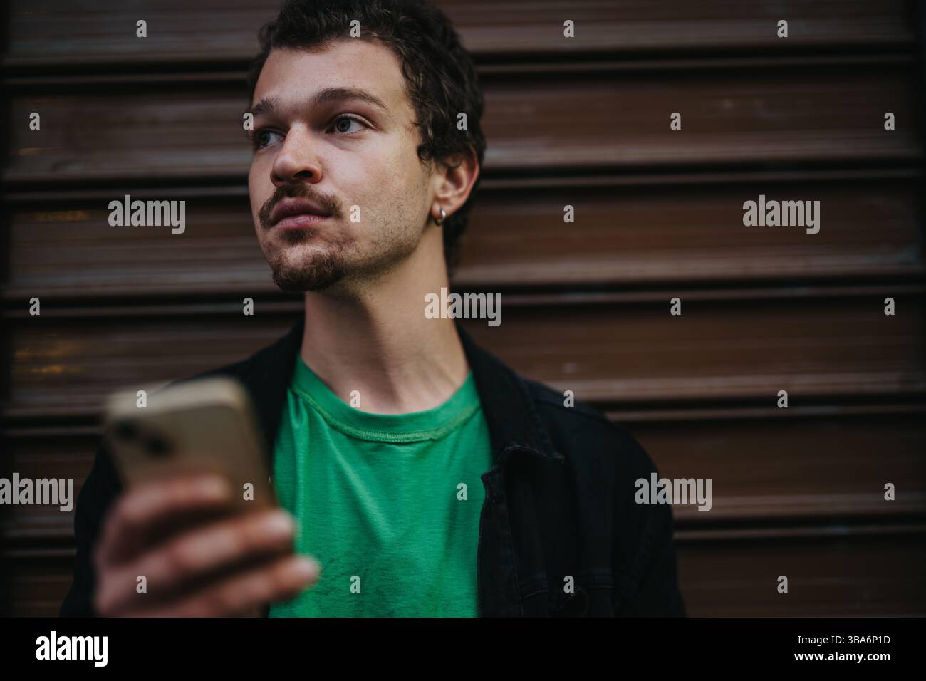 Jeune homme tenant son téléphone intelligent semble réfléchi dans un cadre urbain de rue Banque D'Images