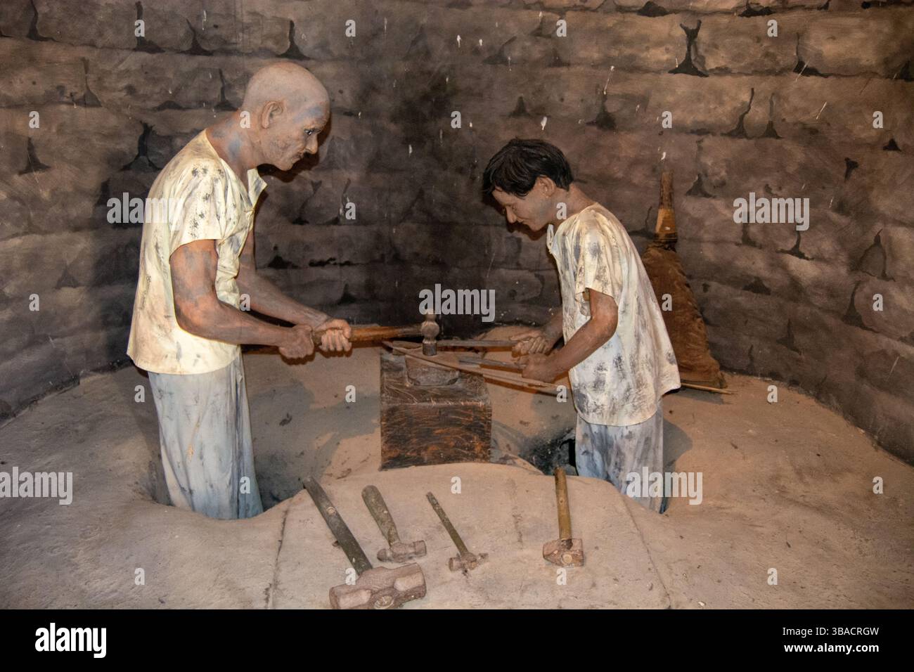 Deux sculptures grandeur nature d'hommes travaillant dans un cadre historique, utilisant des outils pour façonner des matériaux. L'environnement ressemble à un atelier muré de pierre, w Banque D'Images