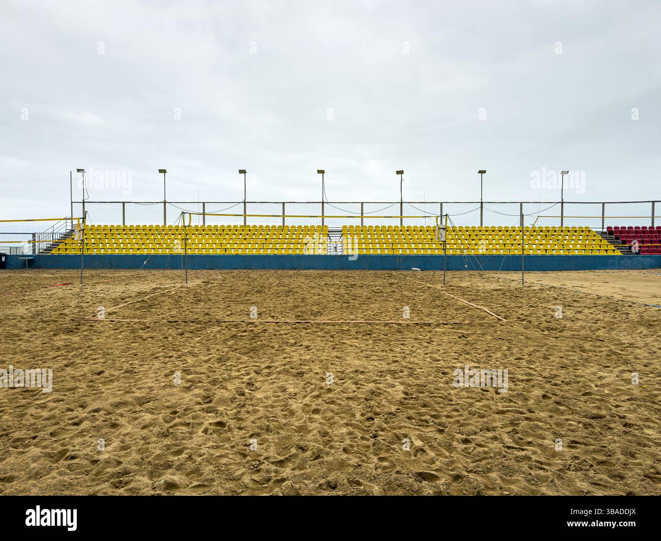 Terrain de Beach volley vide avec sièges étagés sous le ciel nuageux. Surface de sable, composition symétrique, pas de personnes. Lieu sportif, loisirs d'été. Banque D'Images