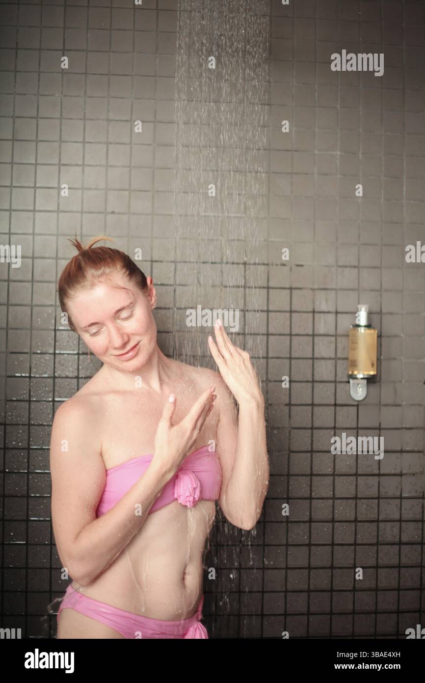 Jeune femme sous le ruisseau d'eau chaude dans une salle de douche spa moderne. Banque D'Images