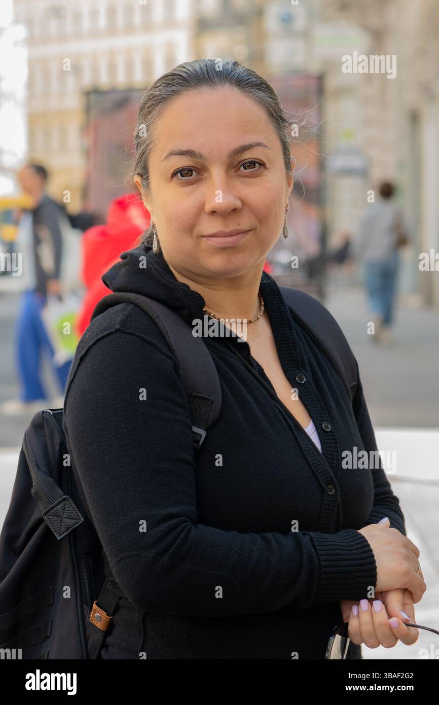 Une femme d'âge moyen avec un sac à dos sourit dans une rue de la ville Banque D'Images