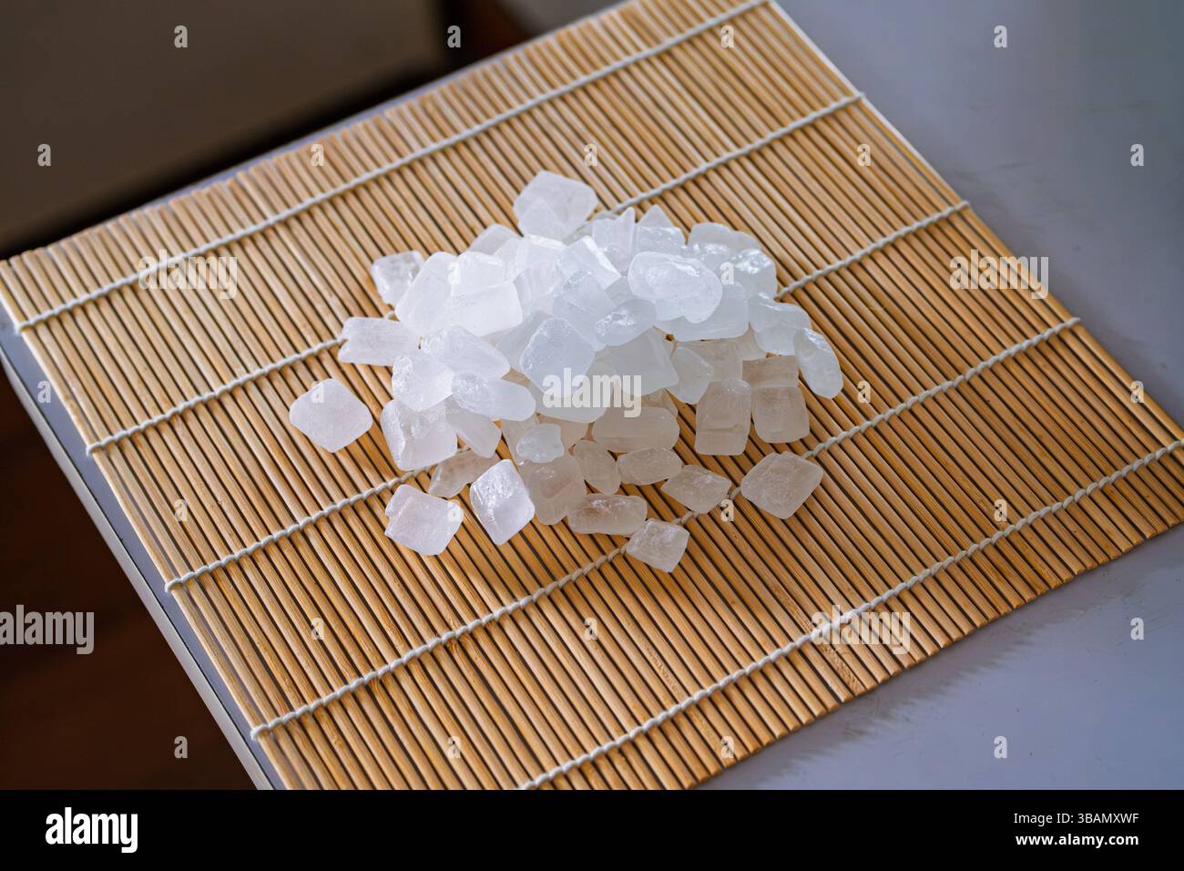 Gros plan d'une collection de cristaux de sucre de roche blancs et clairs empilés sur un tapis à roulettes de sushi en bambou brun clair. Banque D'Images