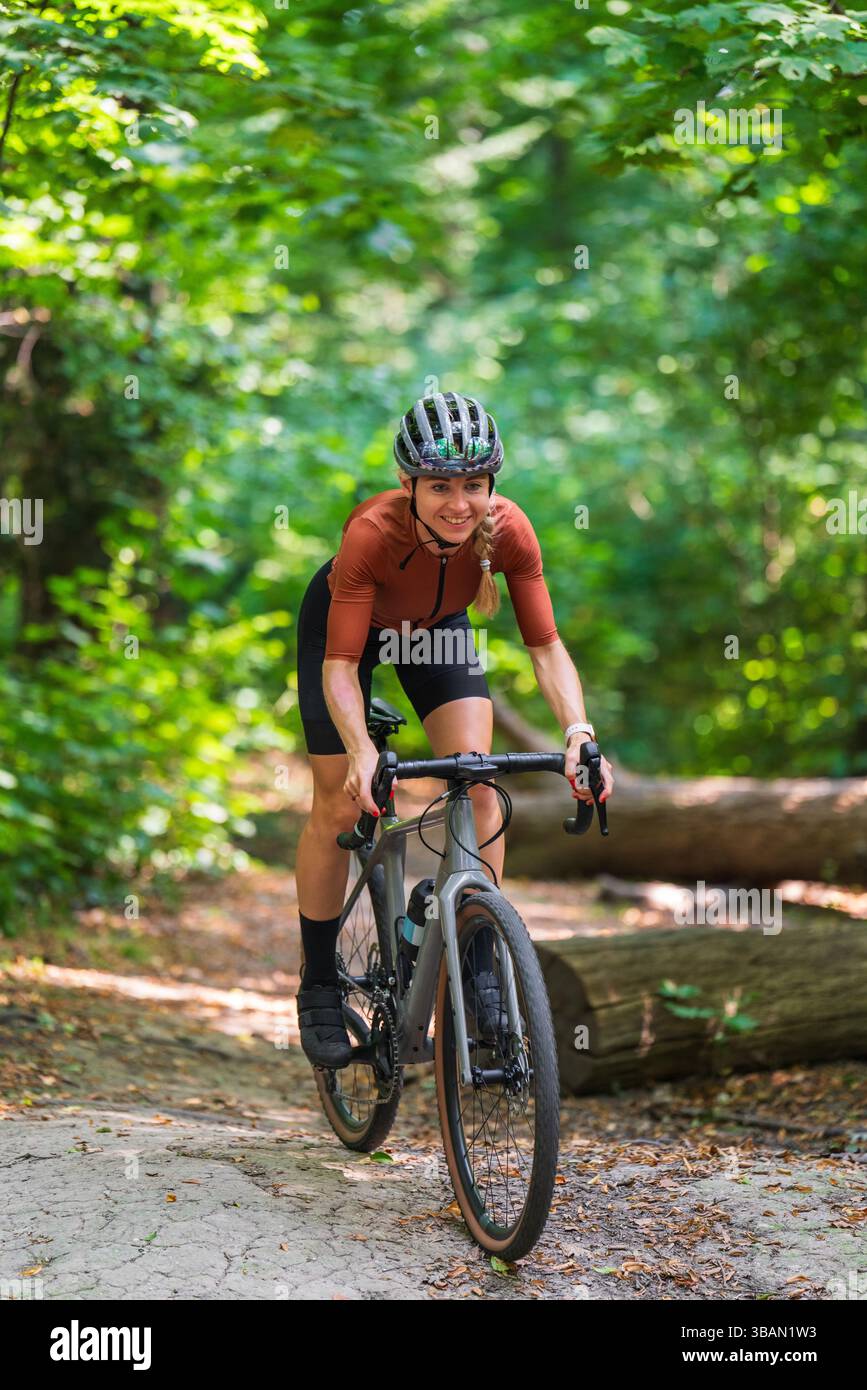 Cycliste féminine souriante portant une tenue de sport et un casque fait du vélo de gravier le long du sentier forestier. Concept d'aventure en plein air, cyclisme à travers la nature, an Banque D'Images