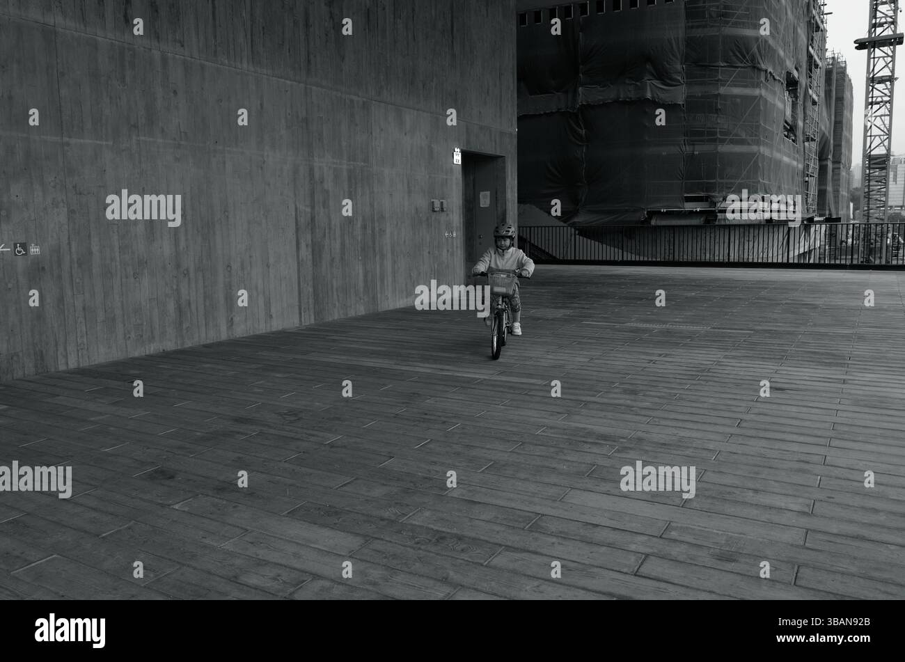 Enfant conduisant un vélo dans un couloir en béton ouvert devant le musée M+ Banque D'Images