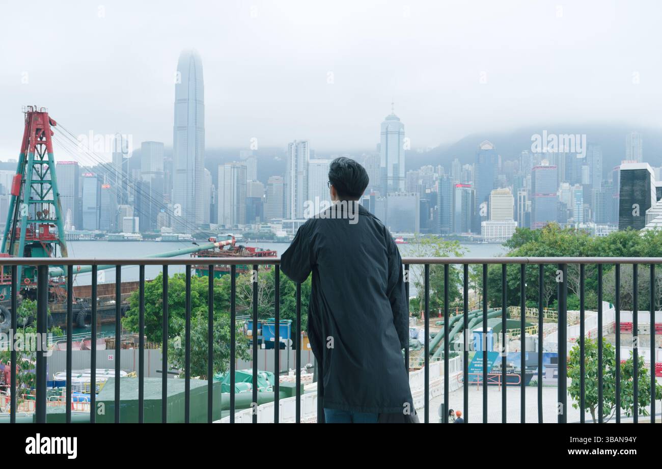 L'homme regarde à travers le port Victoria à l'horizon de la ville depuis une terrasse par un après-midi brumeux Banque D'Images