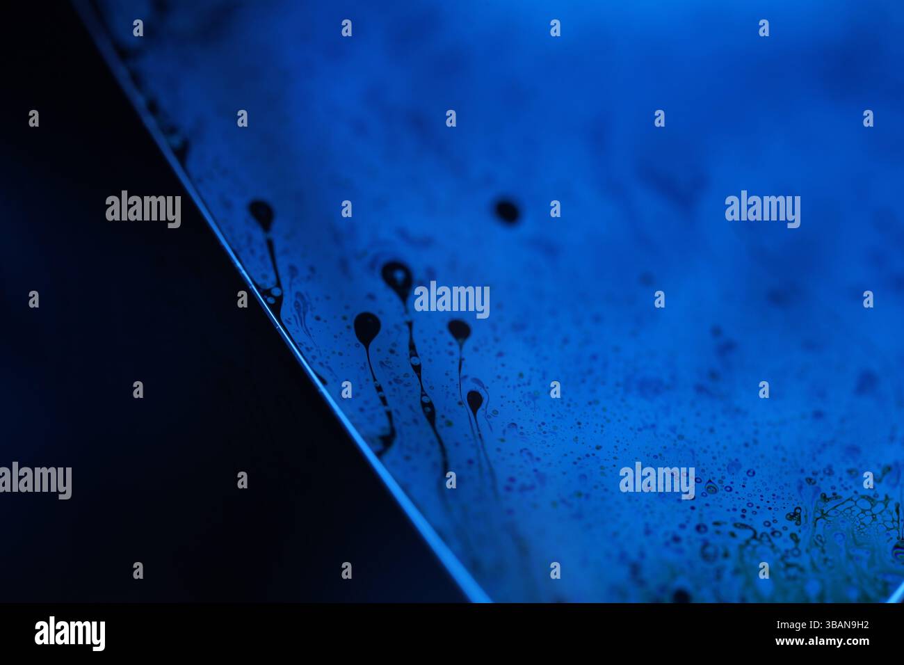 Surface liquide bleu profond sur fond noir, mouvement des taches d'huile, chimie brillante, fond surréaliste, couleur bleu ciel Banque D'Images