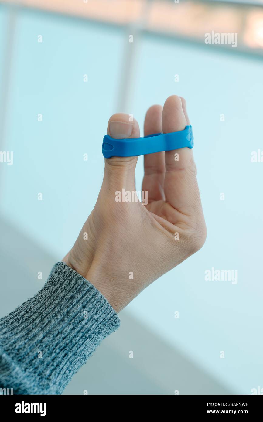 gros plan d'un homme utilisant une bande élastique bleue pour exercer ses doigts et les muscles de son avant-bras Banque D'Images