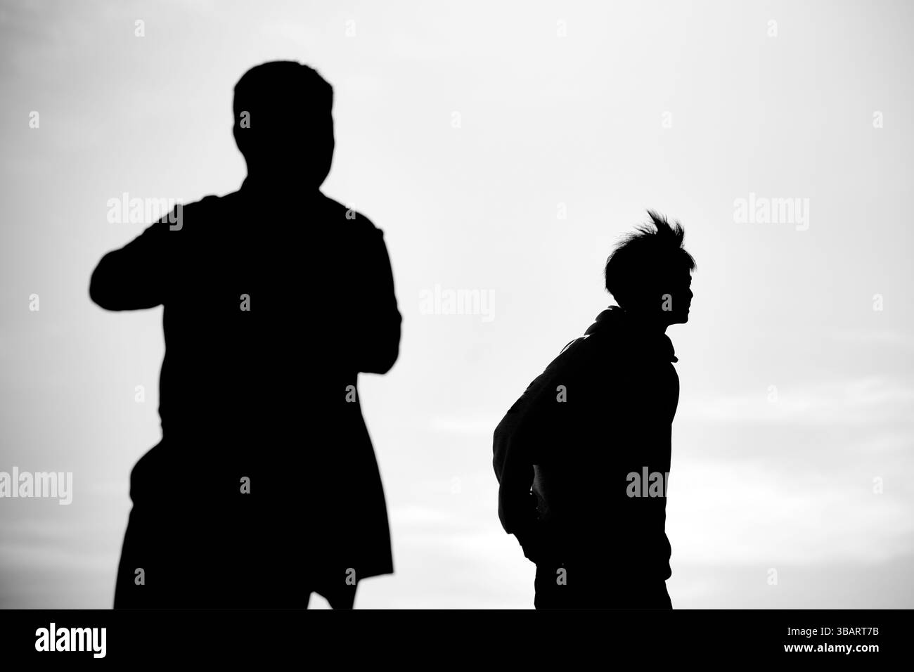 Deux hommes silhouettes se tiennent dans des directions opposées, divisés par la lumière et l'espace, créant une métaphore visuelle de la déconnexion. Banque D'Images