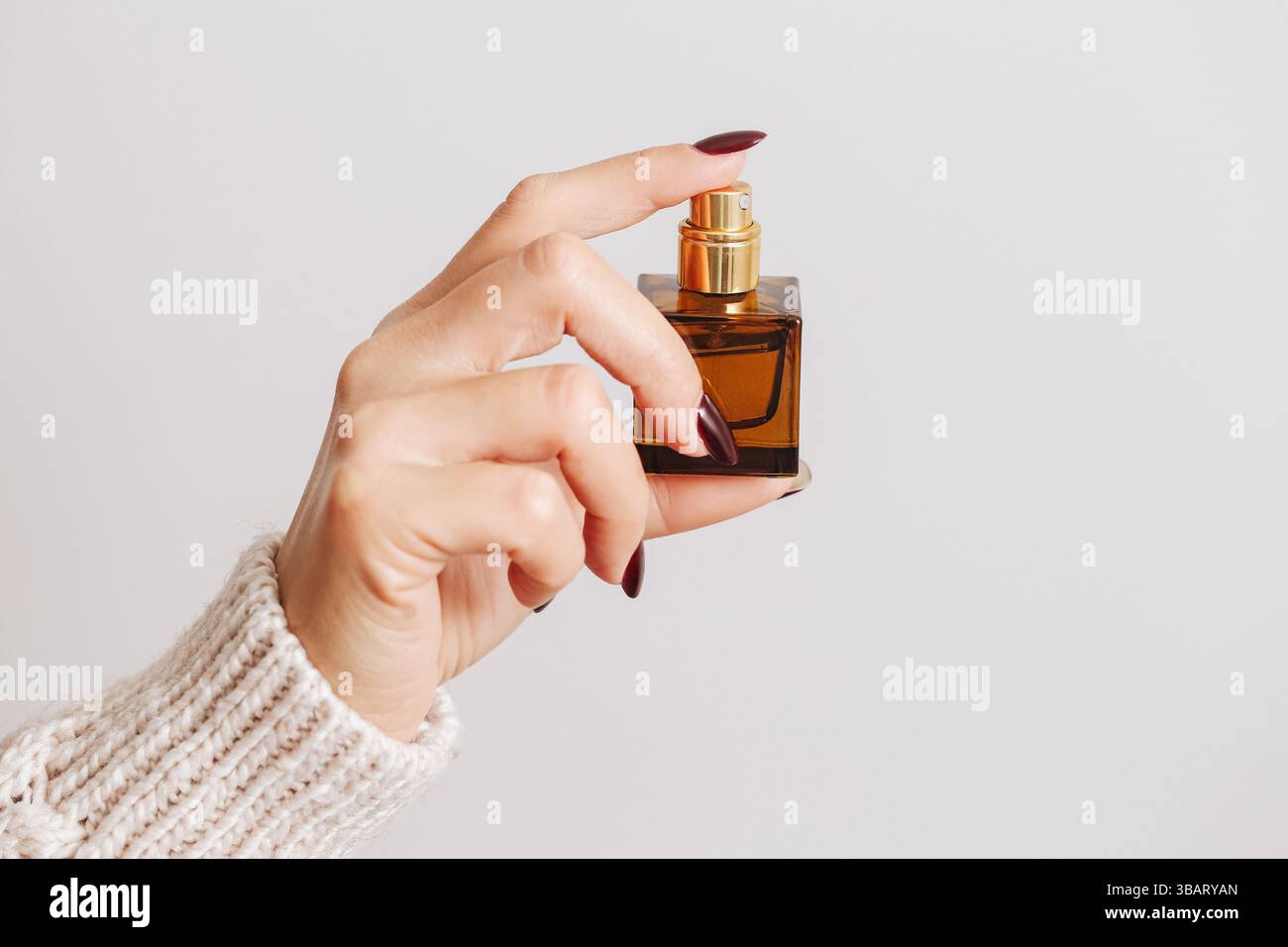 Main de femme tenant bouteille de parfum. Récipient pulvérisateur en verre brun. Produit de beauté sur fond blanc. Concept cosmétique minimal élégant de soin de la peau. Banque D'Images