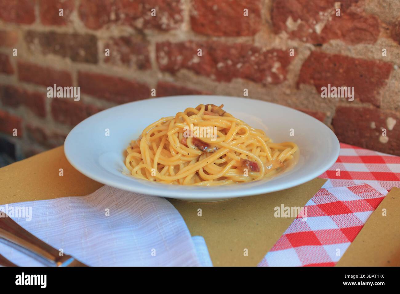 Une assiette de pâtes fraîchement préparées se trouve sur une table dans un restaurant italien confortable. Les tons chauds du mur de briques rustique complètent l'invitation Banque D'Images