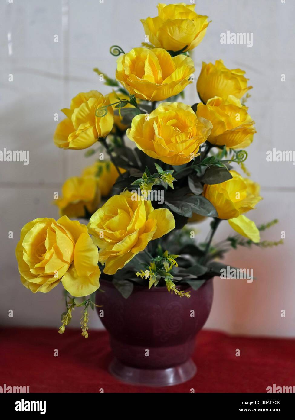 Une délicieuse collection de fausses roses jaunes présentées dans un vase rouge à des fins décoratives - Image de stock capturée avec un smartphone