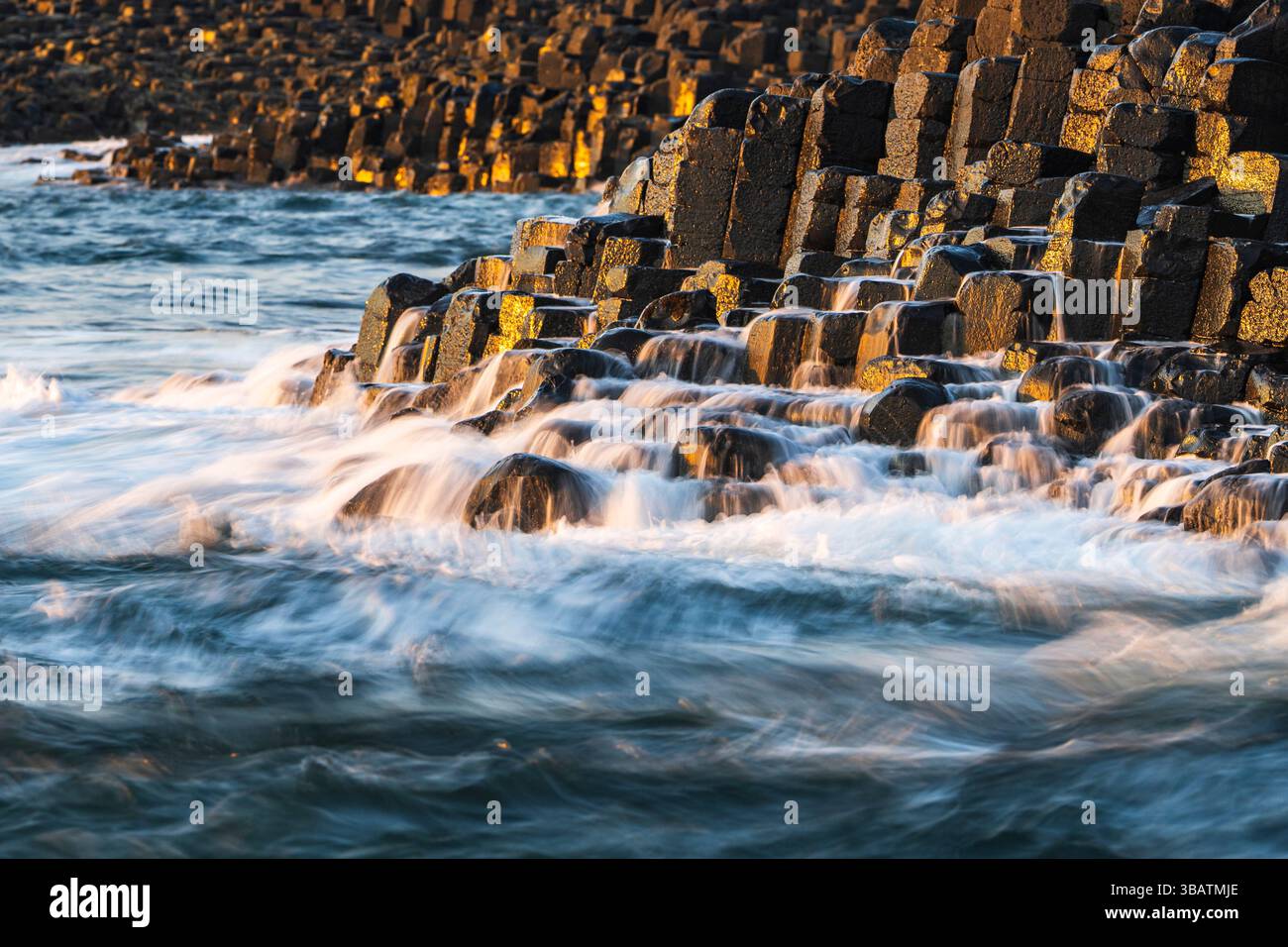 Lumière du soleil en fin d'après-midi sur les colonnes de basalte de Grand Causeway, avec des vagues qui s'écoulent d'eux. Chaussée des géants, côte d'Antrim, Irlande du Nord Banque D'Images