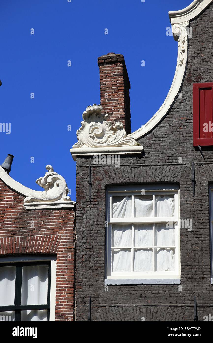 Des pignons en briques se rapprochent avec des ornements sculptés, une fenêtre et une cheminée contre un ciel bleu à Amsterdam, quartier Jordaan, pays-Bas, mai 2025. Banque D'Images