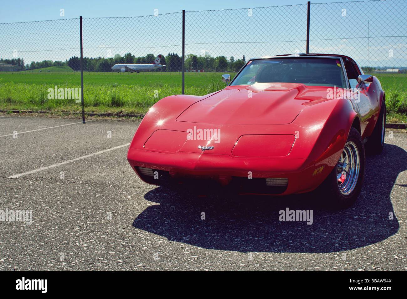 Classic Red Chevrolet Corvette C3 garé devant la clôture de l'aérodrome avec avion en arrière-plan le jour ensoleillé Banque D'Images