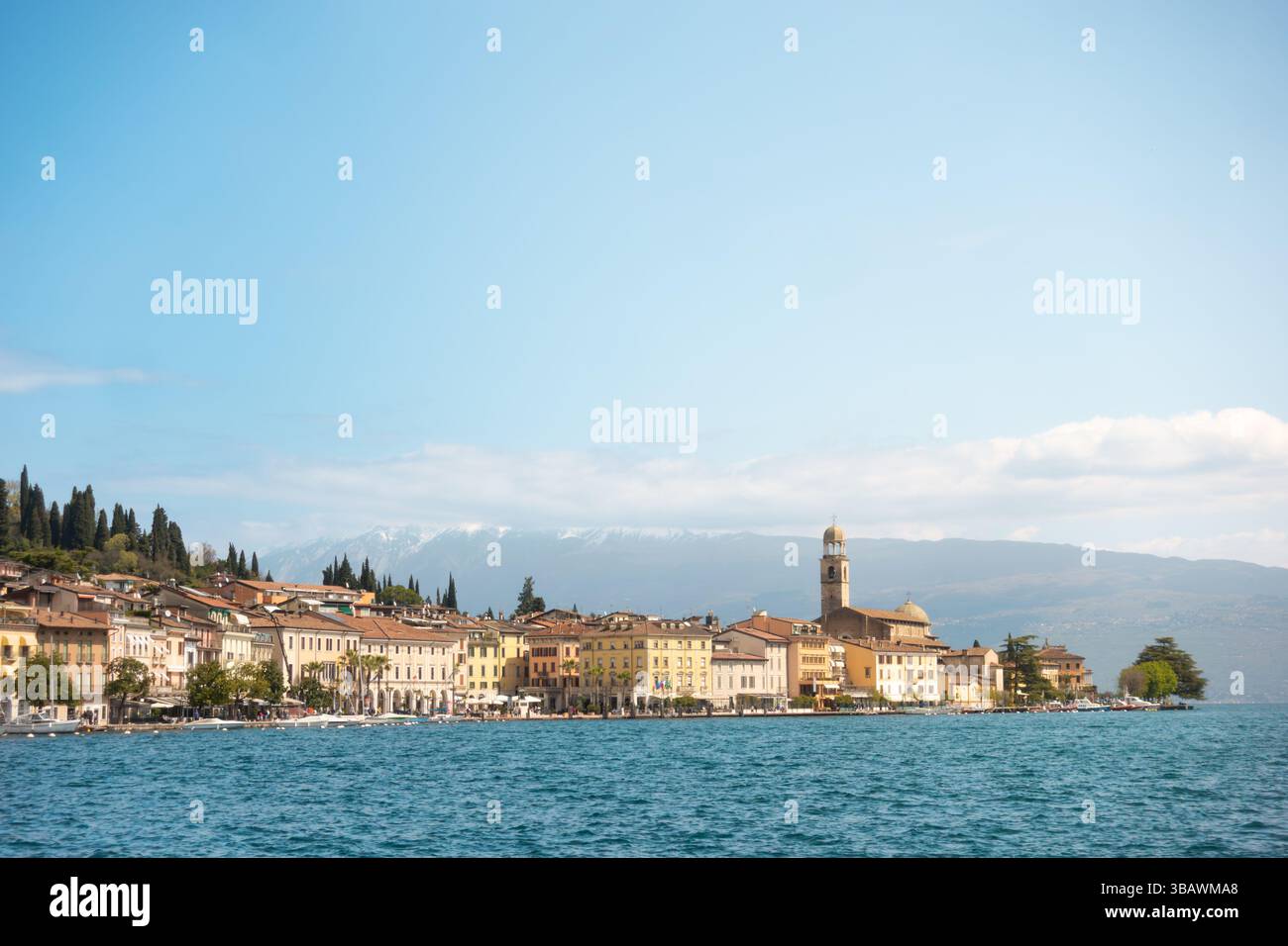 Vue panoramique de la ville côtière de Salò par le lac Lago di Garda avec tour d'église emblématique en face des montagnes des alpes en arrière-plan par temps clair Banque D'Images
